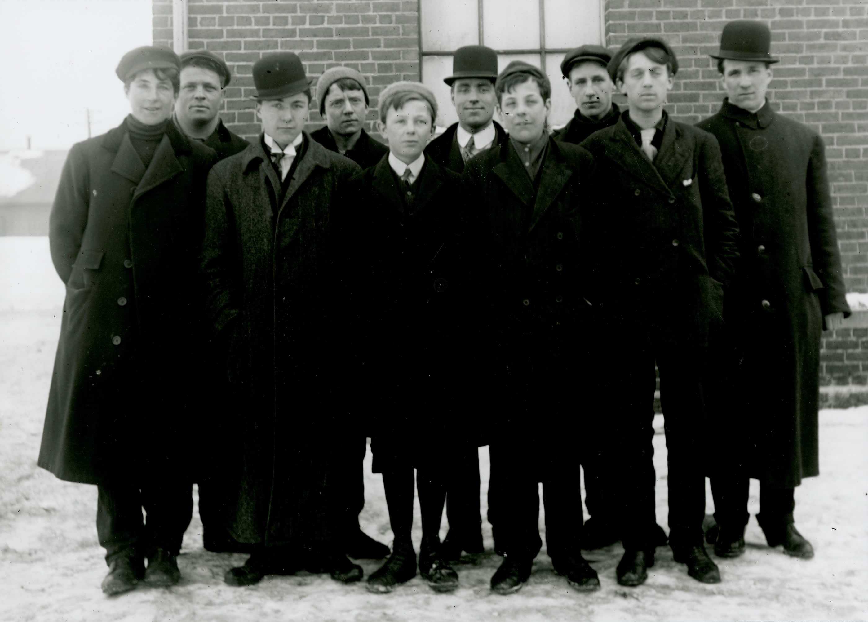 Photographie en noir et blanc - Dix hommes en tenue civile attendent ensemble sur un sol enneigé; la plupart se montrent enthousiastes.